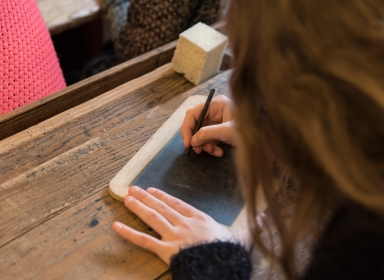 Pige skriver med griffel på lille tavle i "Den Gamle Skolestue" 